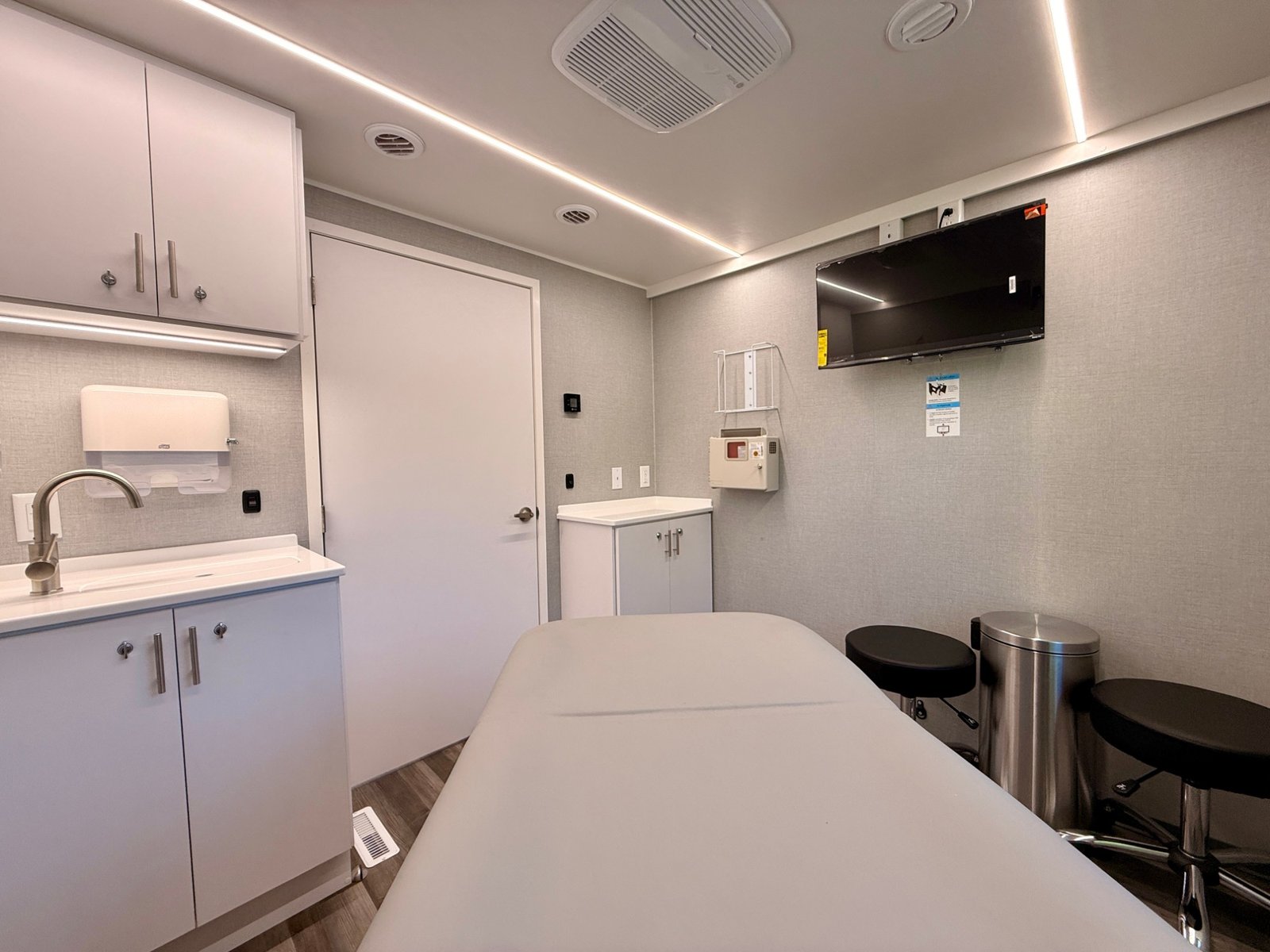 Exam room with treatment table, wall-mounted monitor, sink, and clinical storage